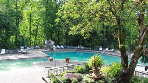 A swimming pool with lounge chairs, surrounded by trees and a decorative fountain. - Sauna + Hot Tub | Mtn Views | Pet-Friendly Cabin (Gatlinburg)