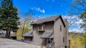 A two-story house with a front porch, a small attached garage, and a clear blue sky. - Sauna + Hot Tub | Mtn Views | Pet-Friendly Cabin (Gatlinburg)