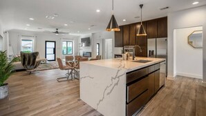A modern kitchen with a marble island, stainless steel appliances, and pendant lighting. - Arthouse · Arthouse, Modern Luxury Getaway w/ Hot Tub near DT (Houston)