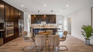A modern kitchen with dark wood cabinets, stainless steel appliances, and a central island with seating. - Arthouse · Arthouse, Modern Luxury Getaway w/ Hot Tub near DT (Houston)