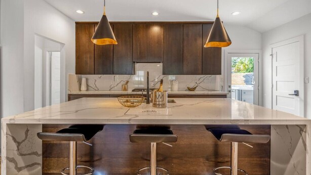 A modern kitchen with dark wooden cabinets, a marble countertop, and two pendant lights. - Arthouse · Arthouse, Modern Luxury Getaway w/ Hot Tub near DT (Houston)