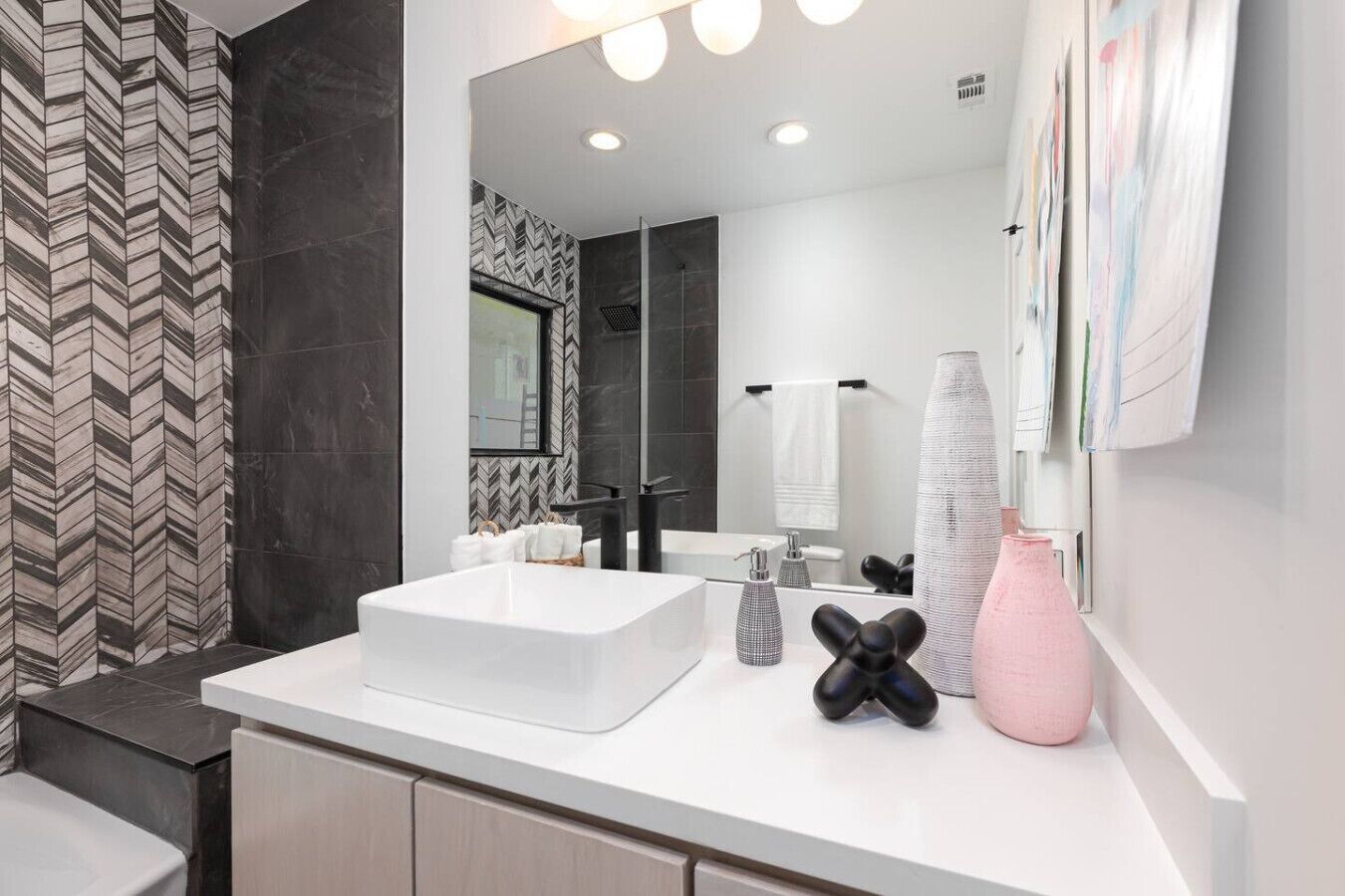 A modern bathroom with a large mirror, a white sink, and a black and pink vase.