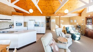 Een moderne keuken met witte kasten en een centraal eiland, een gezellige zithoek met een bank en fauteuils, en een meterkast met boekenplanken.