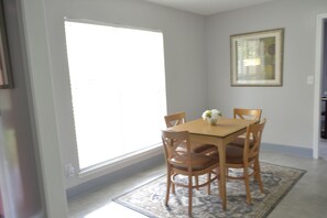 Un coin repas avec une table et des chaises, une fenêtre et un tableau encadré au mur.