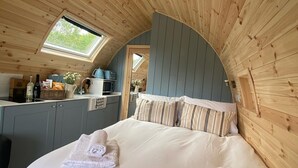 Une chambre confortable avec un plafond en bois, une lucarne, un lit avec du linge de maison blanc et une petite kitchenette.