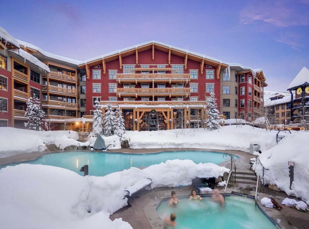Ein Hotel mit Pool, umgeben von Schnee, Holzbalkonen und einem großen Gebäude im Hintergrund.