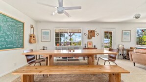 Un comedor amplio con una mesa de madera y bancos, una pizarra con dibujos, una guitarra y un ventilador de techo.