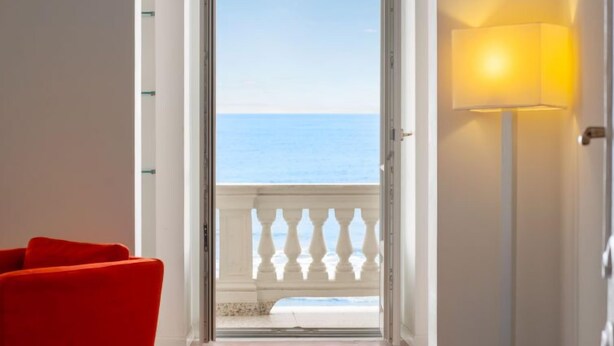 A room with a red chair, a white lamp, and a view of the sea through an open door. - Beach House by Interhome (Alassio)
