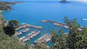A marina with numerous boats docked, surrounded by clear blue water and a distant island. - Beach House by Interhome (Alassio)