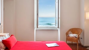 A bedroom with a large window overlooking the sea, a red bed, and a wicker chair. - Beach House by Interhome (Alassio)