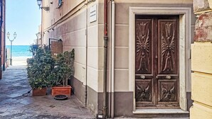 A narrow cobblestone street with a building featuring a large, ornate wooden door and potted plants. - Beach House by Interhome (Alassio)