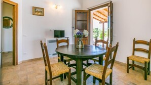 Un comedor con una mesa redonda, cuatro sillas de madera, un jarrón con flores, un televisor sobre un mueble bajo y un techo de madera.