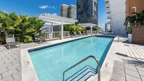 A rooftop pool with a pergola, palm trees, and high-rise buildings in the background.