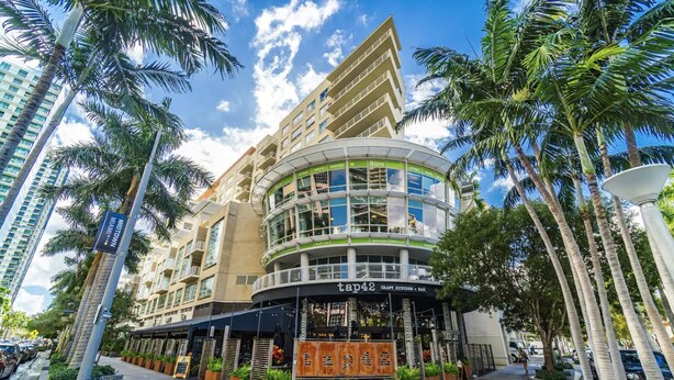 A multi-story hotel with a curved glass facade, outdoor seating area, and palm trees.