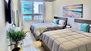 A modern bedroom with two beds, a large window, a painting, and a potted plant.