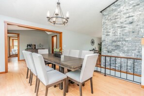 A dining area with a wooden table and chairs, a chandelier, and a brick wall.