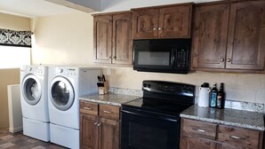 A kitchen with wooden cabinets, a microwave, a stove, and a washing machine. - 2 bedroom holiday home (Tropic)