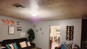 A living room with a brown sofa, a coffee table, and a patterned rug. There is a plant, a wall with decorative items, and a doorway leading to another room. - 2 bedroom holiday home (Tropic)