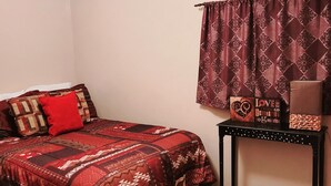 A bedroom with a bed, a bedside table, a lamp, a window with patterned curtains, and a ceiling light. - 2 bedroom holiday home (Tropic)