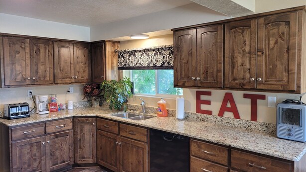A kitchen with wooden cabinets, granite countertops, a dishwasher, and a large window with a view of greenery. - 2 bedroom holiday home (Tropic)