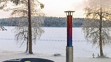 A snowy landscape with a tall, narrow structure in the center, surrounded by leafless trees and a frozen body of water.