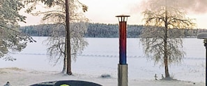 A snowy landscape with a tall, narrow structure in the center, surrounded by leafless trees and a frozen body of water. - Urpola riviera by Interhome (Rovaniemi)