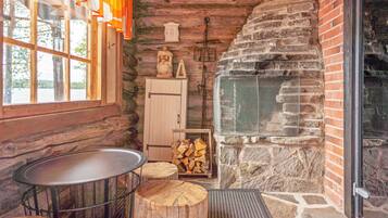 A rustic cabin interior with a stone fireplace, wooden walls, a metal table, and a window with curtains.