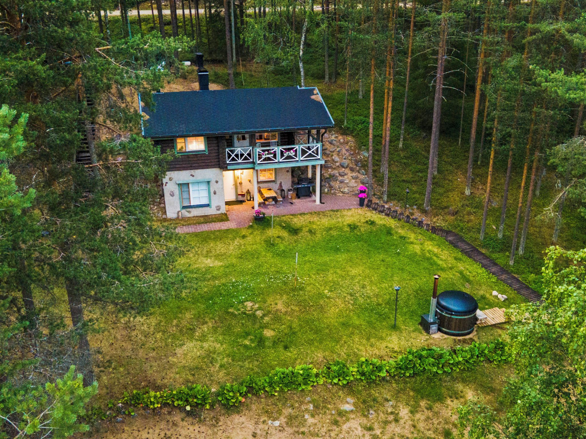 A two-story house with a dark roof, surrounded by a forest.