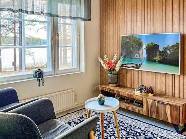 A living room with a sofa, a small round table, a TV mounted on a wooden wall, and a window with curtains. - Urpola riviera by Interhome (Rovaniemi)