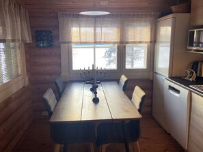 A wooden interior with a dining table, chairs, a refrigerator, and a window with curtains. - Urpola riviera by Interhome (Rovaniemi)