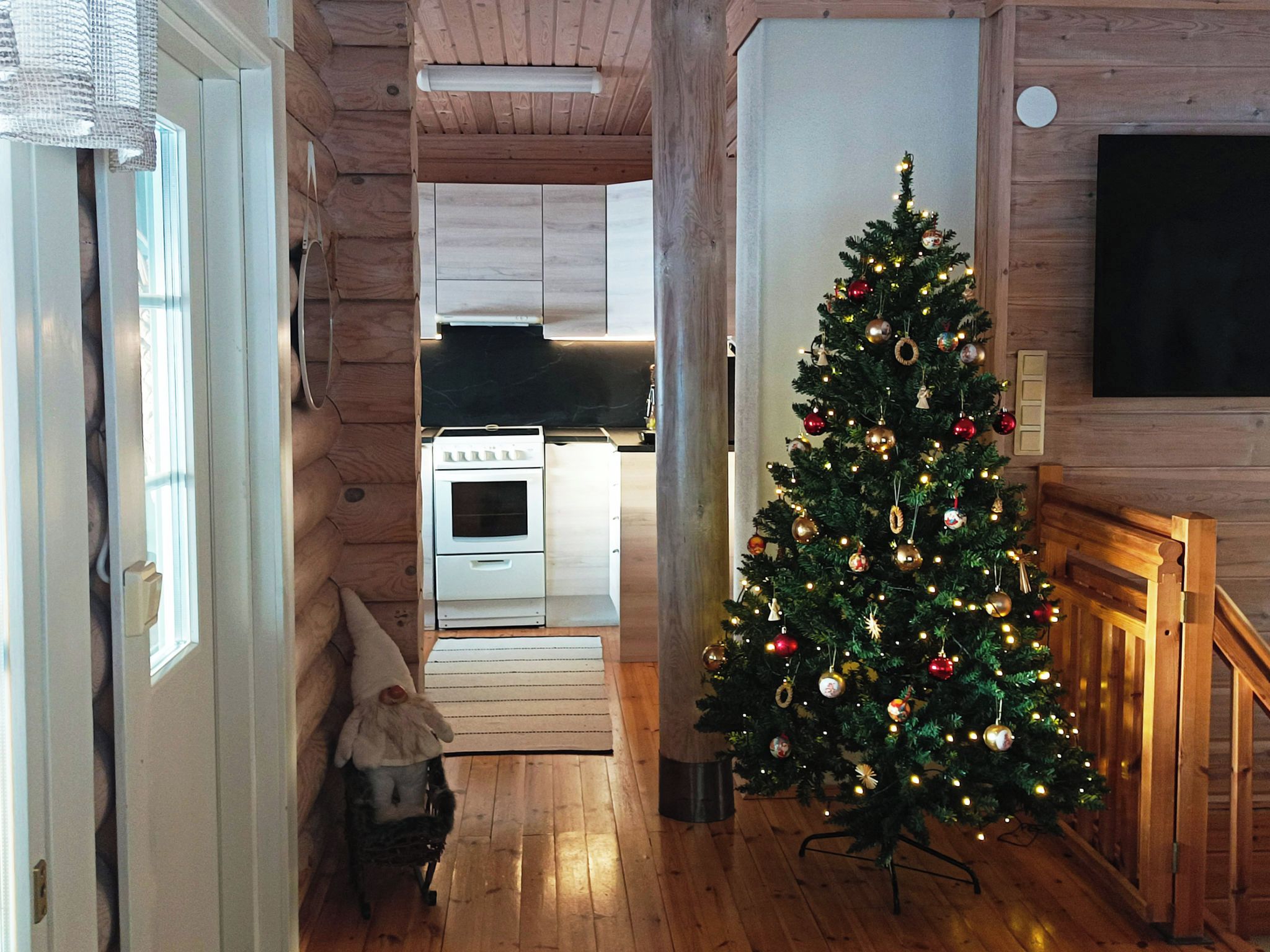 Ein Holzinterieur mit einem Weihnachtsbaum, einer Küche im Hintergrund und einem an der Wand befestigten Fernseher.
