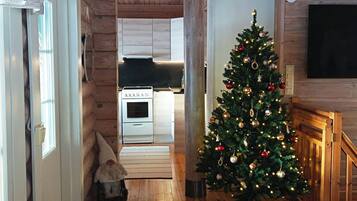Ein Holzinterieur mit einem Weihnachtsbaum, einer Küche im Hintergrund und einem an der Wand befestigten Fernseher.