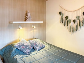 A bedroom with a bed, pillows, a wall-mounted shelf with a tree decoration, bedside lamps, and a wall hanging. - Urpola riviera by Interhome (Rovaniemi)