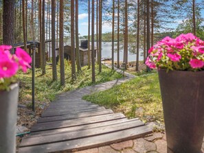 A wooden pathway leading to a cabin by a lake, surrounded by tall trees.