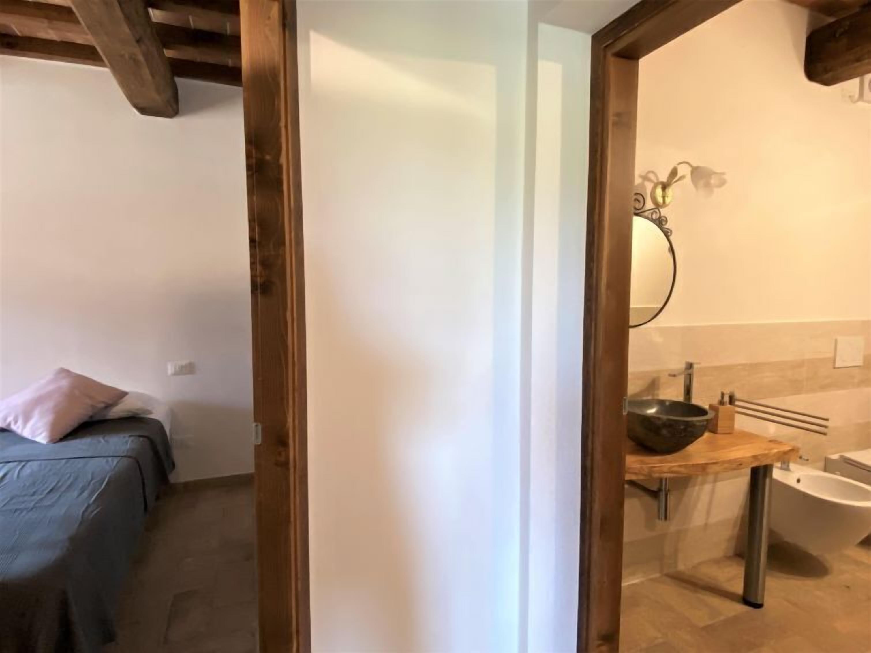 Une chambre à coucher avec un lit, une porte en bois et une salle de bain comprenant un lavabo, un miroir et un bidet.