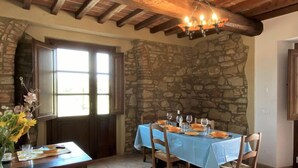 Un coin repas agrémenté d’un mur en pierre, de poutres en bois au plafond et d’une table dressée pour quatre personnes.