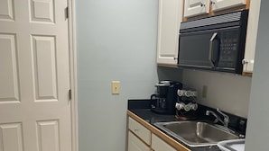 A compact kitchen with white cabinets, a black microwave, a coffee maker, and a stainless steel sink. - Sea Trail Golf and Beach Get Way (Sunset Beach)
