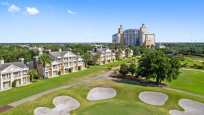 A golf course with bunkers and a large hotel with multiple stories and balconies. - Beautiful Townhome with Golf Course Views | Near Attractions (Kissimmee)