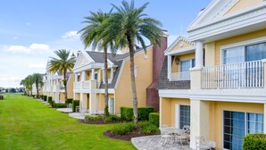 A row of modern townhouses with balconies, a well-maintained lawn, and a patio area with outdoor furniture. - Beautiful Townhome with Golf Course Views | Near Attractions (Kissimmee)