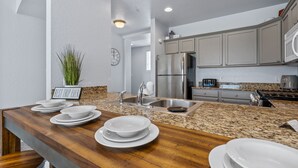 A modern kitchen with granite countertops, stainless steel appliances, and a wooden dining area. - Beautiful Townhome with Golf Course Views | Near Attractions (Kissimmee)