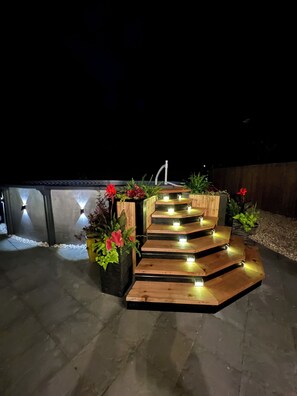 A wooden outdoor staircase with integrated lighting, surrounded by potted plants and flowers.