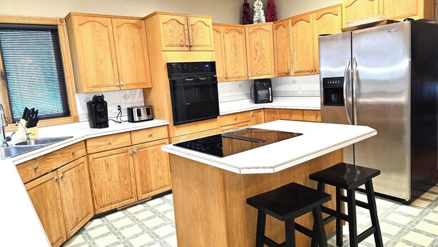 Una cucina moderna con mobili in legno, un frigorifero in acciaio inossidabile, un forno integrato, un microonde e una grande isola con sgabelli.