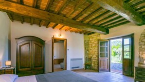 A bedroom with a bed, wooden wardrobe, stone wall, and a door leading to a balcony. - Apartment Olea by Interhome (Guardistallo)