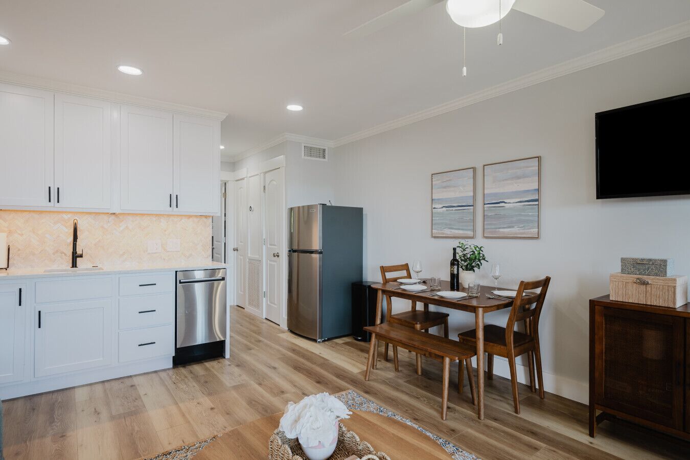 A modern kitchen with white cabinets, a stainless steel refrigerator, and a dining area with a wooden table and chairs.