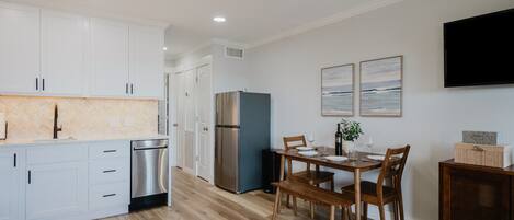A modern kitchen with white cabinets, a stainless steel refrigerator, and a dining area with a wooden table and chairs.