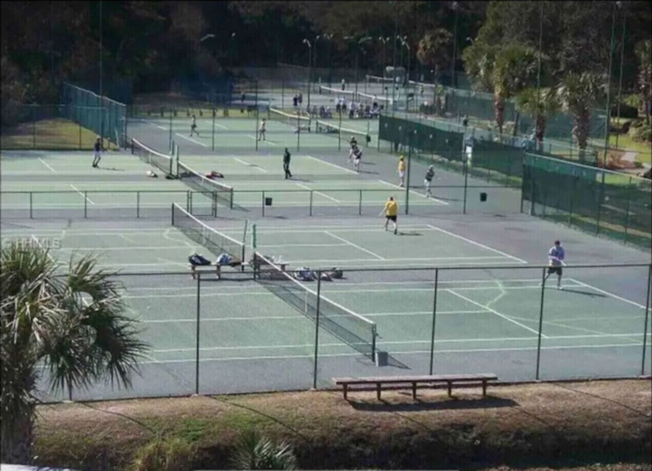 A tennis court with multiple courts, benches, and a fence.