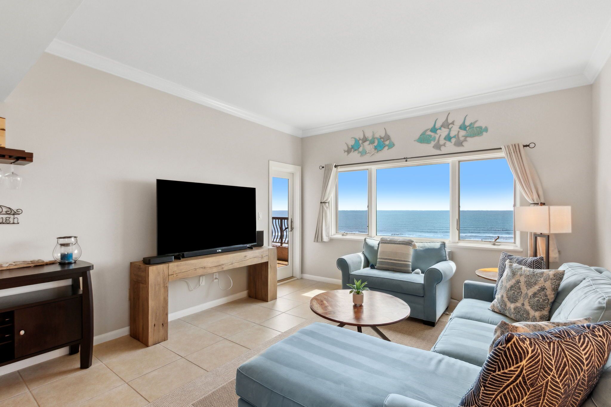 Una sala de estar con televisor, sofás, una mesa de centro y vista al mar.