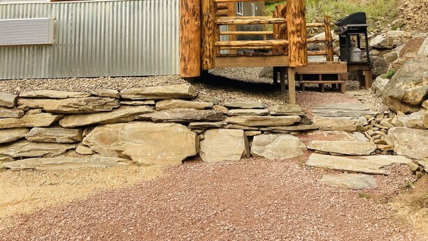 A log cabin with a stone foundation, a metal door, and a wooden gate. - 8 miles to Mount Rushmore - Sleeps 2 - King Bed (Rapid City)