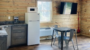 A cozy cabin with a kitchen area featuring a refrigerator, microwave, and coffee maker. There is a dining table with chairs, a ceiling fan, and a large window providing natural light. - 8 miles to Mount Rushmore - Sleeps 2 - King Bed (Rapid City)