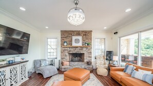 A spacious living room with a stone fireplace, leather sofas, a large flat-screen TV, and a chandelier.